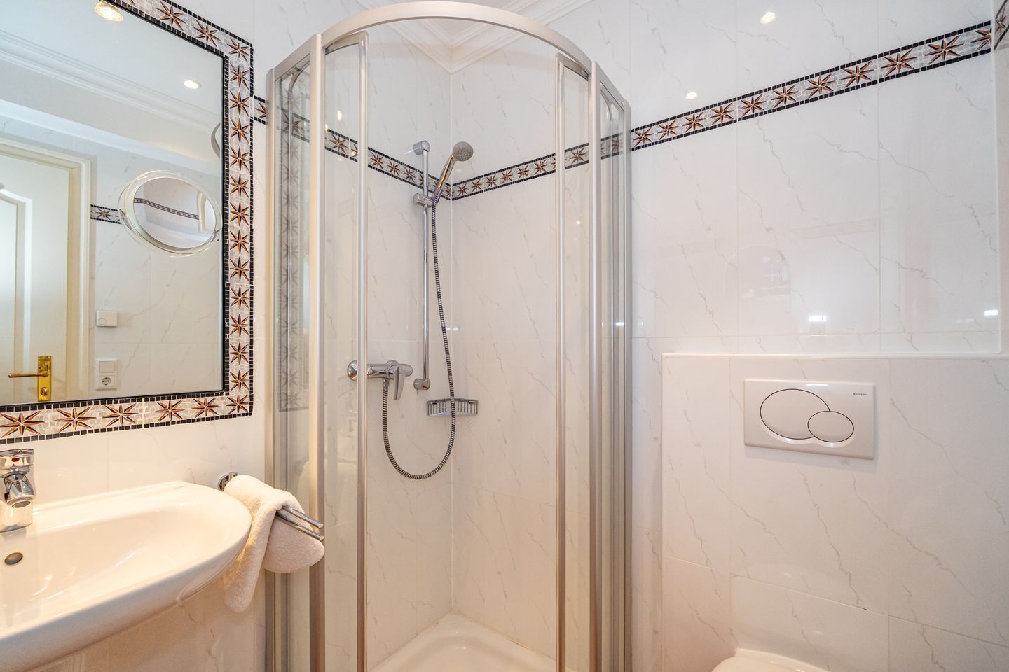 Une salle de bain moderne dotée d’une douche à parois de verre, d’un lavabo avec un porte-serviette et d’un miroir orné d’un cadre décoratif.