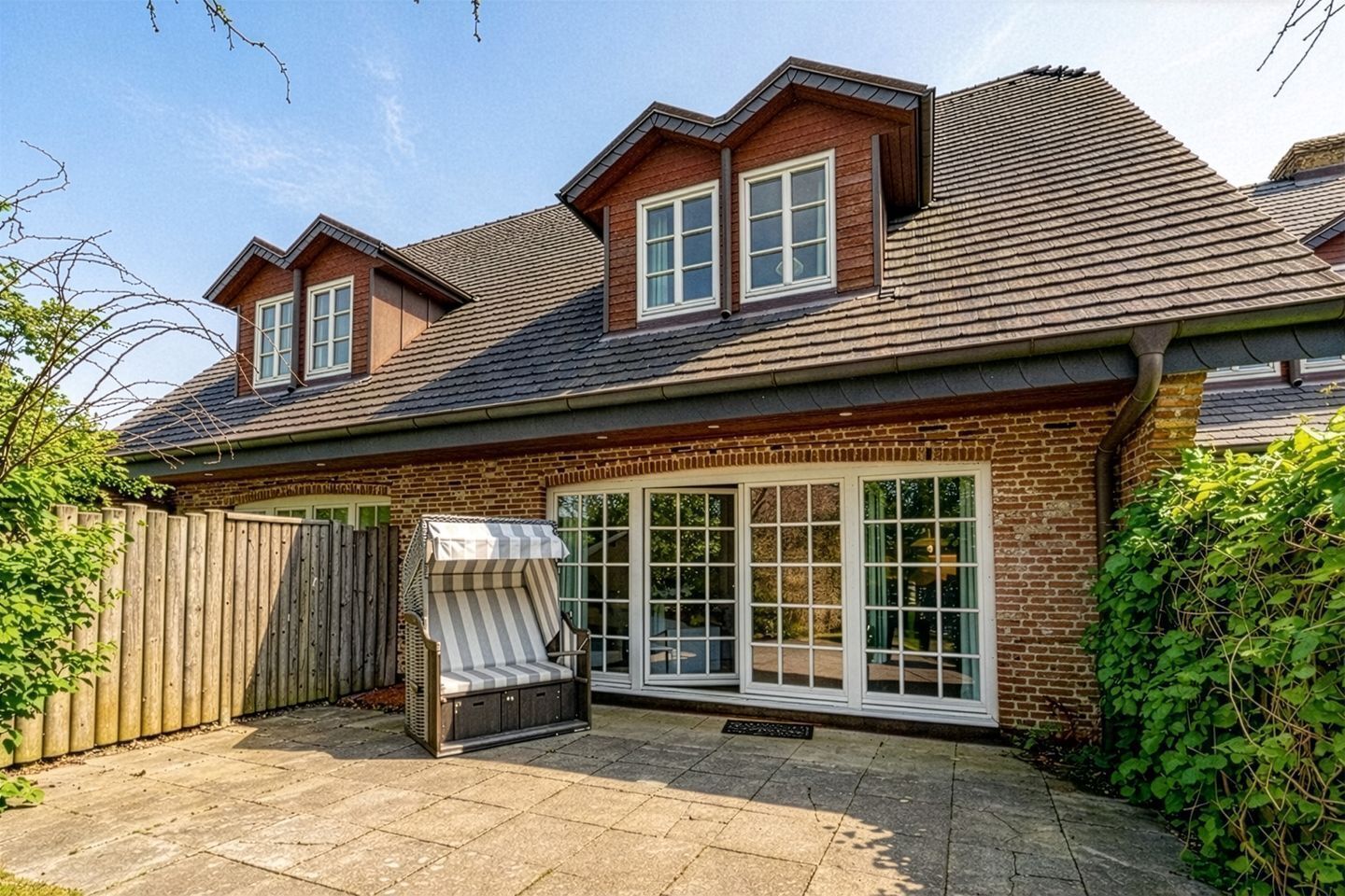 A two-story house with a brick exterior, a large sliding glass door, and a wooden deck.