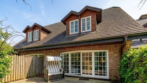 A two-story house with a brick exterior, a large sliding glass door, and a wooden deck. - Senhuk - Senhuk part of the vacation home. With garden and terrace for up to 6 people. (Sylt)