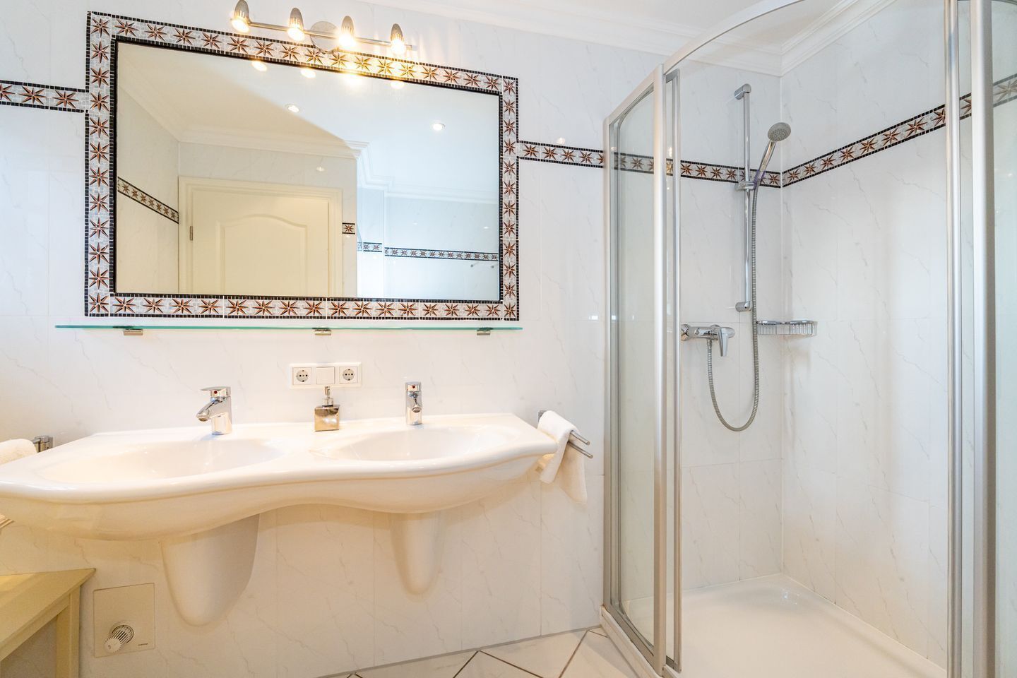 A bathroom with a large mirror, two sinks, a shower, and a tiled backsplash.