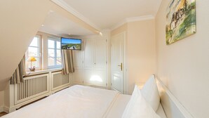 A bedroom with a large bed, a television mounted on the wall, and a window with curtains. - Senhuk - Senhuk part of the vacation home. With garden and terrace for up to 6 people. (Sylt)