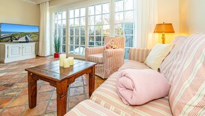 A cozy living room with a wooden coffee table, striped sofas, and a view of the outdoors through large windows. - Senhuk - Senhuk part of the vacation home. With garden and terrace for up to 6 people. (Sylt)