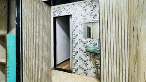 A hallway with a tiled floor, a door, a wall-mounted air conditioner, and a bathroom with a sink and mirror. - Blue Top Dormitory (Mumbai)