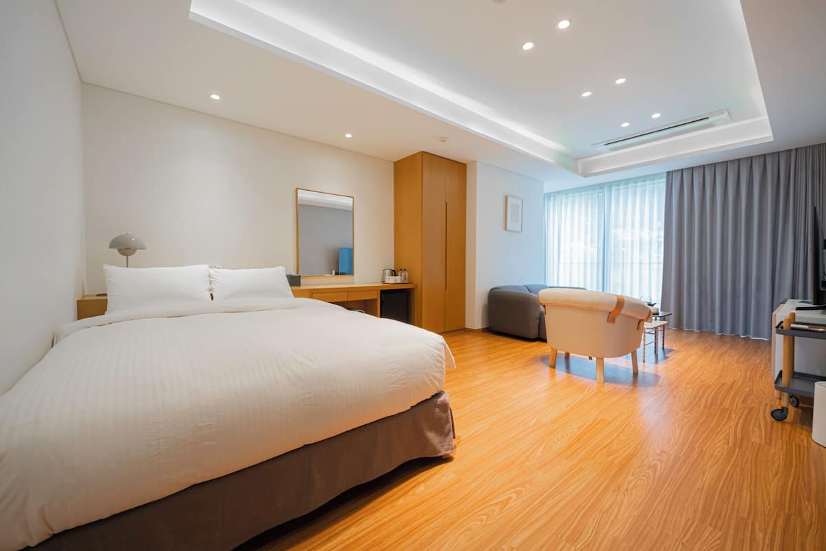 Una habitación de hotel moderna con una cama grande, un escritorio, un tocador, una bañera y un ventanal con cortinas.