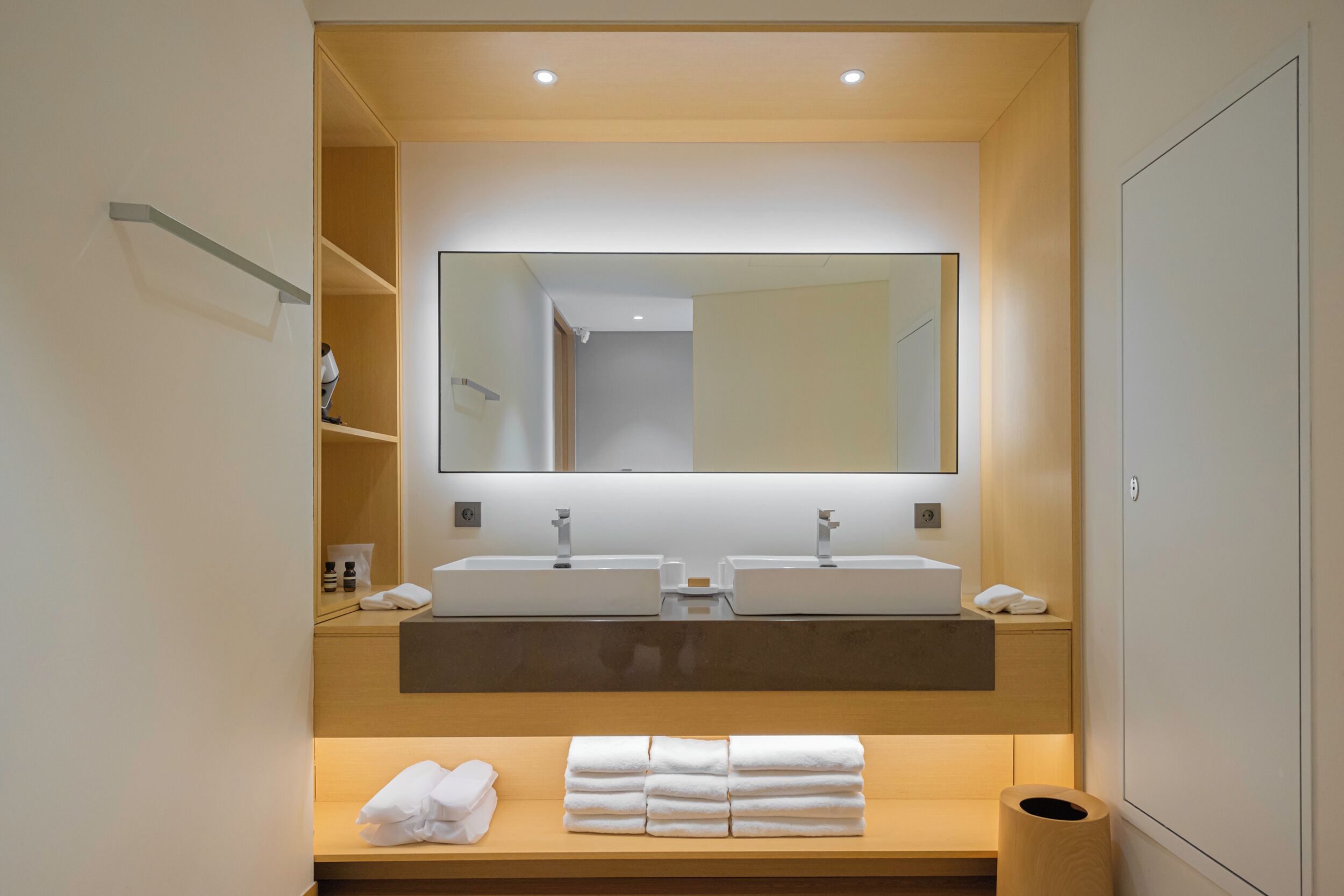 A modern bathroom with two sinks, a large mirror, and neatly folded towels on a wooden shelf.