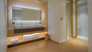 Un baño moderno con un espejo grande, dos lavamanos, un mueble de tocador con toallas y una zona de ducha.
