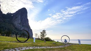 Un sendero que lleva a un mirador con una gran formación rocosa y vista al mar.