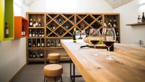 A wine cellar with wooden shelves and bottles, a wooden table with wine glasses, and a corked wine bottle. - Lillil Popping Holiday (Riva del Garda)