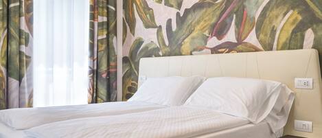 A single bed with white linens in a room with a tropical leaf pattern on the curtains.