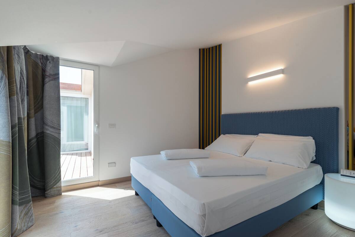Una camera d'albergo moderna con un letto grande, un comodino e vista sul balcone esterno.