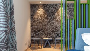 A modern room with a patterned wall, a blue ottoman, and a geometric chair arrangement. - Lillil Popping Holiday (Riva del Garda)