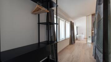 A modern bathroom with a bathtub, wooden flooring, and a black shelving unit with hanging clothes.