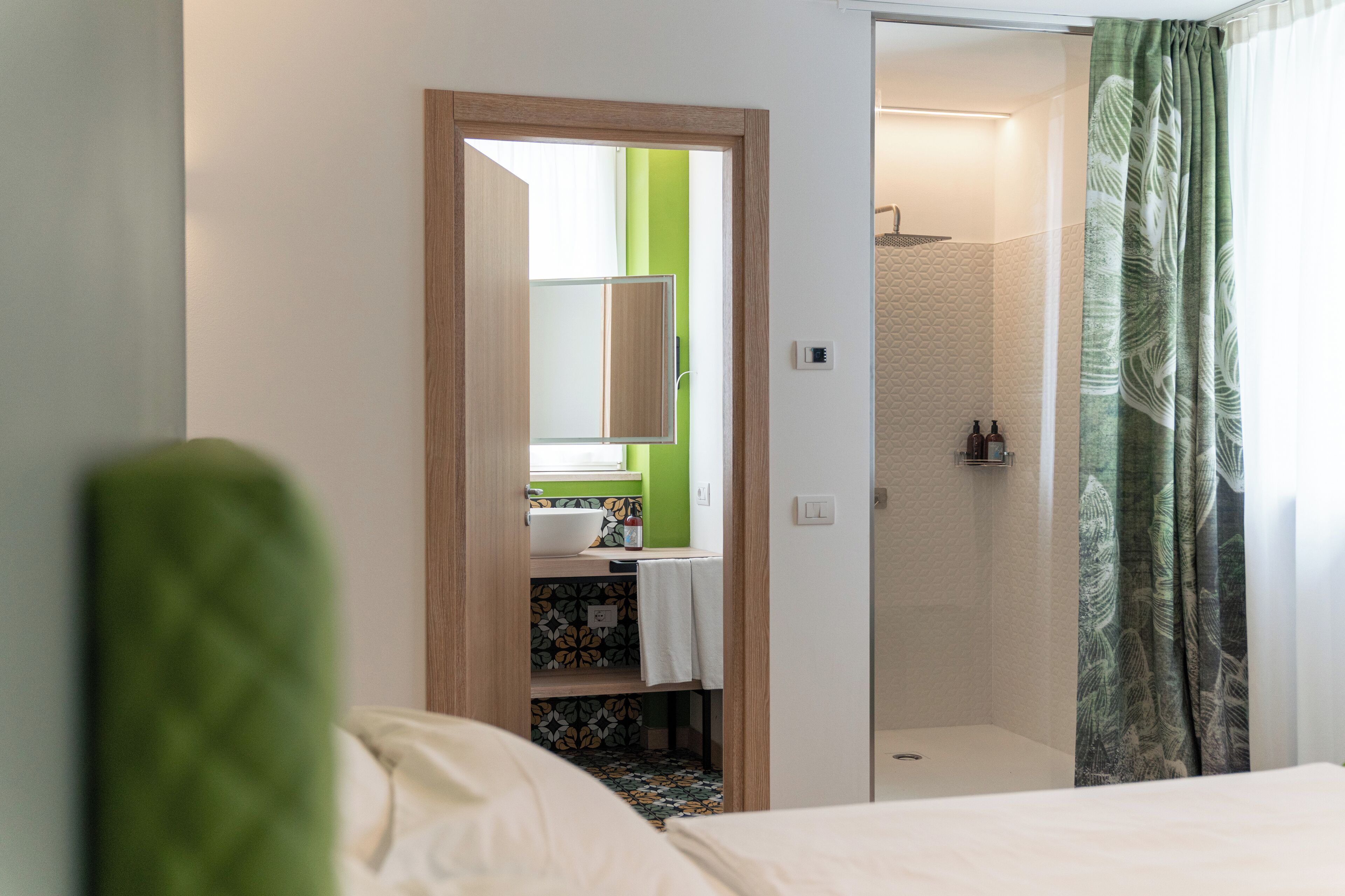 A hotel room with a bed, a bathroom with a shower, and a green accent wall.