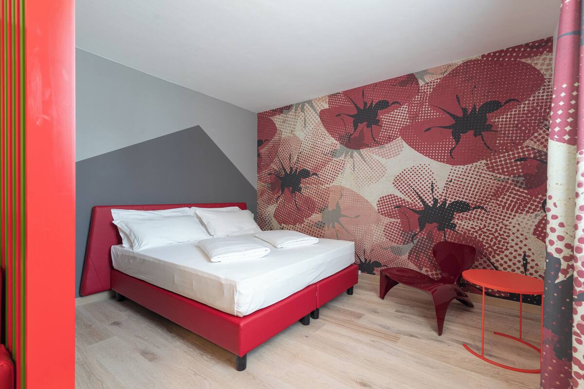 Una camera da letto moderna con un letto rosso, un piccolo tavolino rosso, una sedia rossa e una parete decorata.