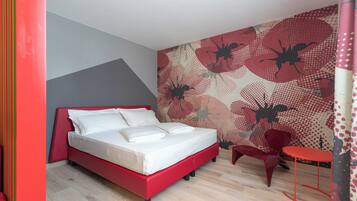 A modern bedroom with a red bed, a small red table, a red chair, and a patterned wall.