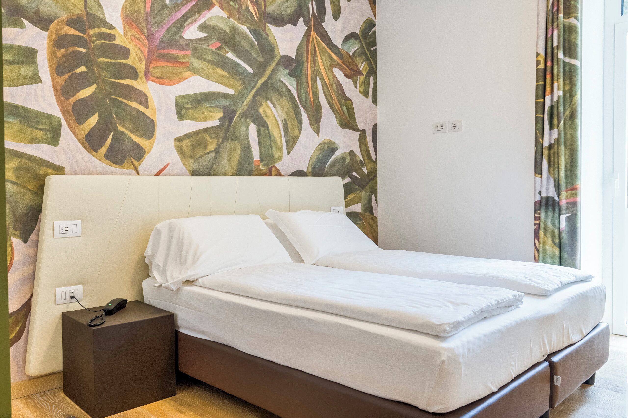 Habitación de hotel con cama, mesita de noche y toma de corriente.