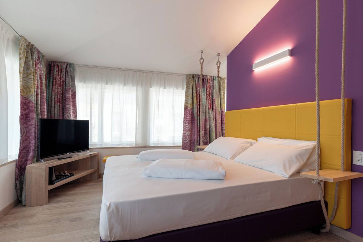 Una camera d'albergo con un letto, una televisione e una finestra con tende.