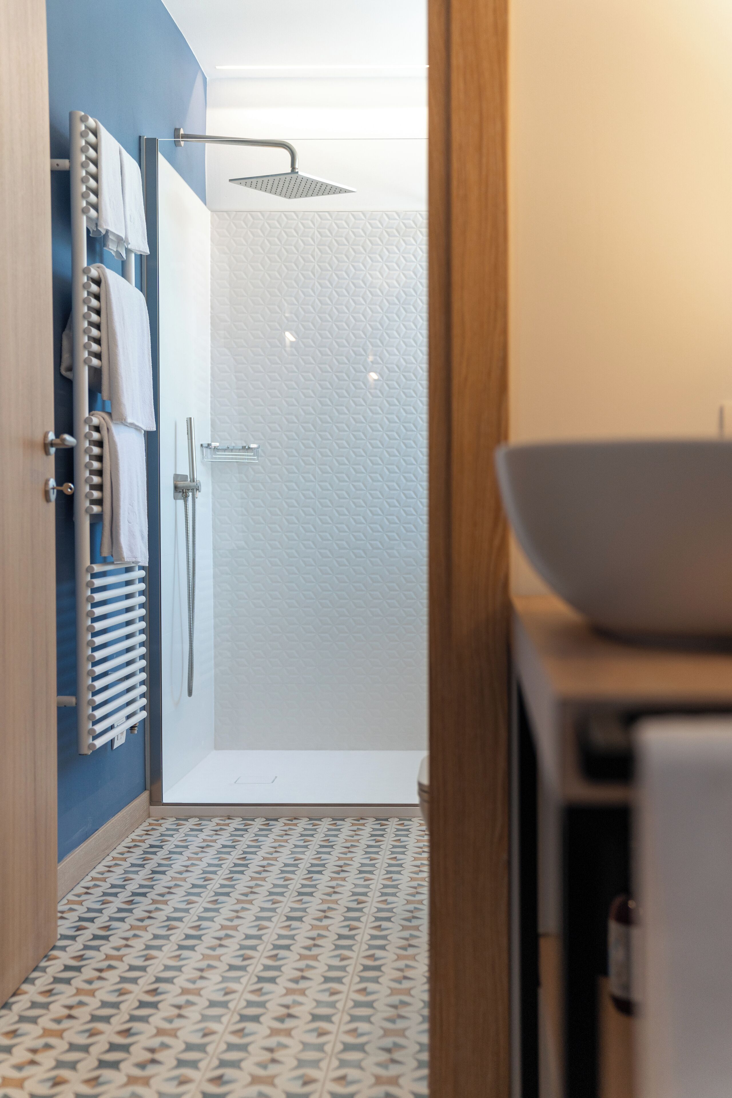 A modern bathroom with a shower, a towel rack, and a patterned floor.