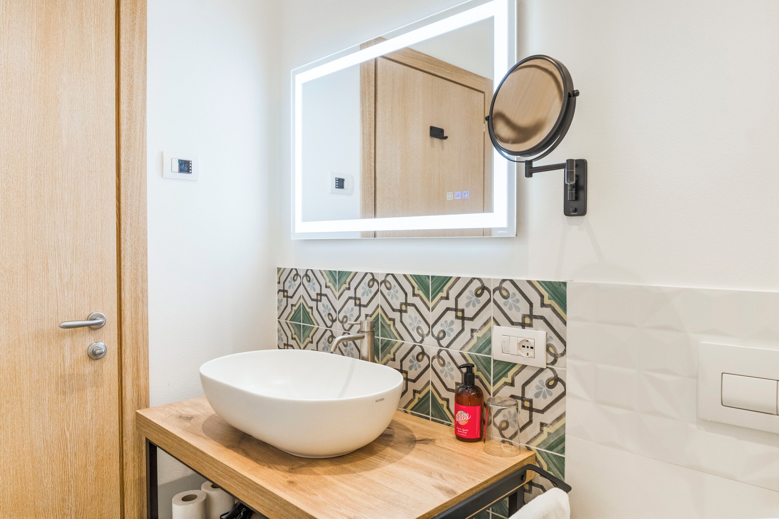 A bathroom with a white sink, a mirror, and a patterned tile backsplash.