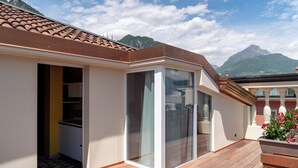 A modern building with a wooden deck, a glass door leading to a kitchen, and a mountain view in the background. - Lillil Popping Holiday (Riva del Garda)
