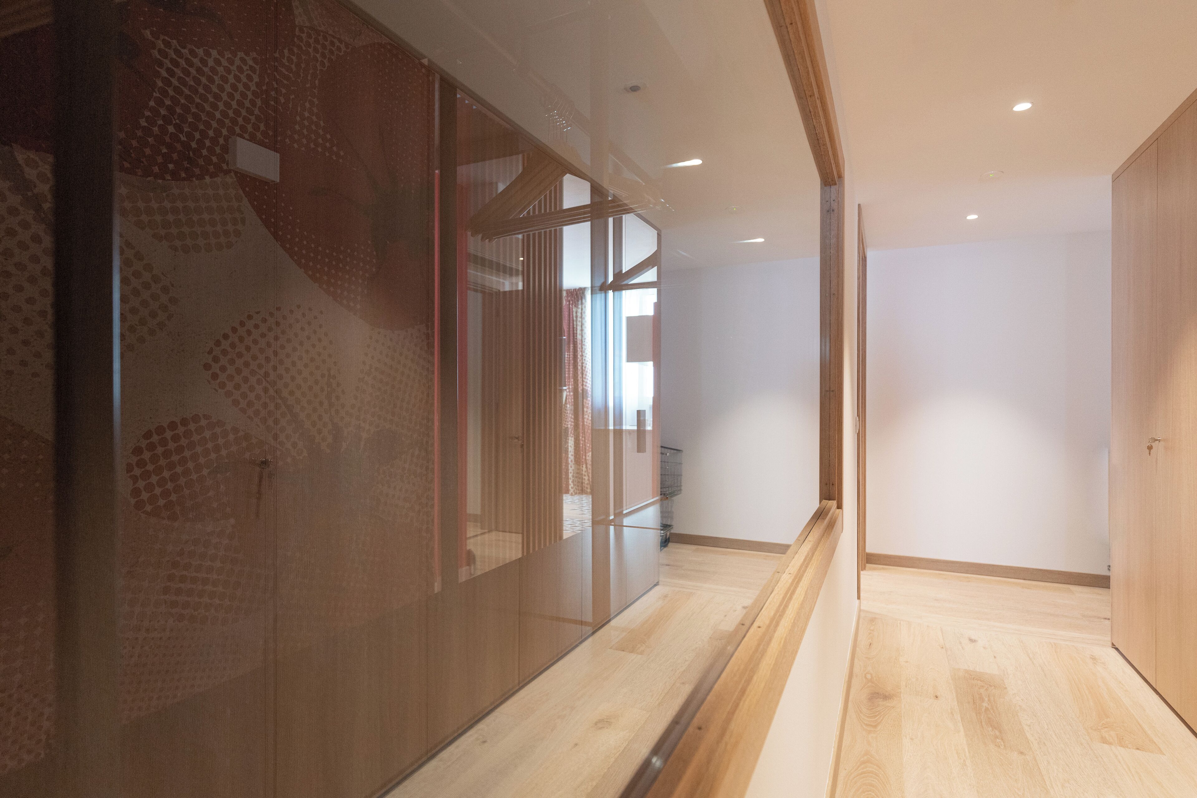 A hallway with wooden flooring, a glass partition with a geometric pattern, and a wooden door.