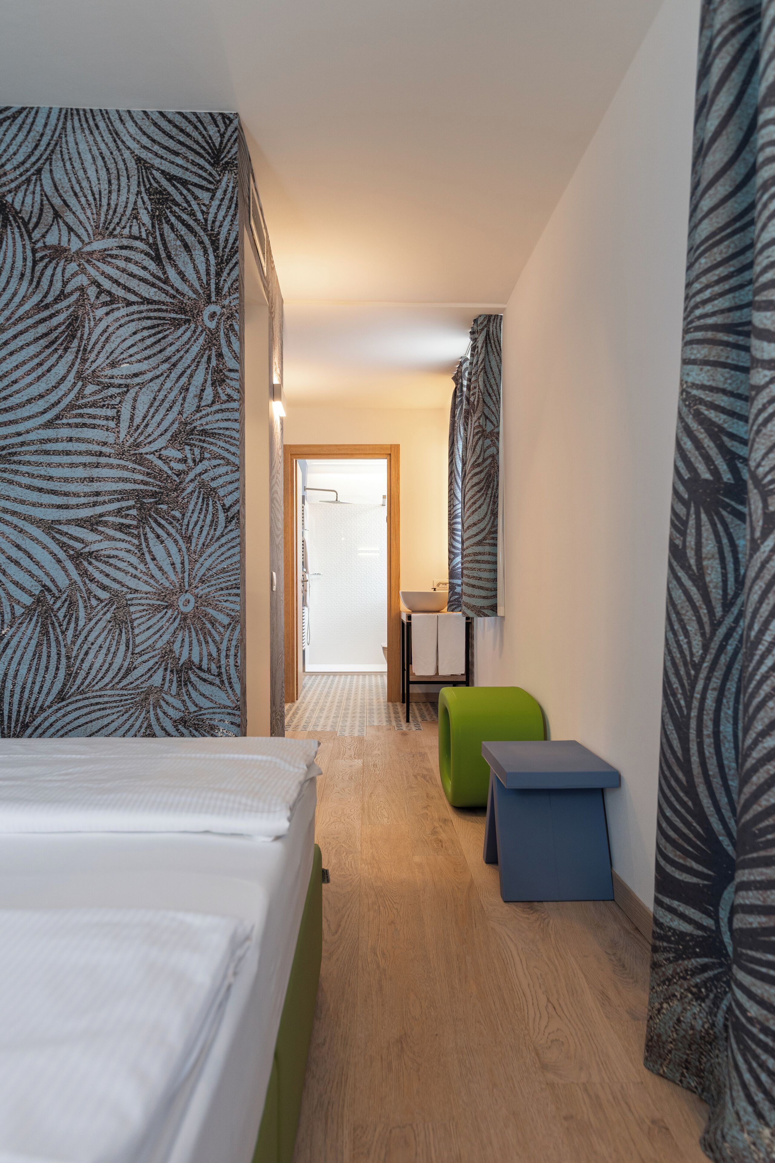 Ein Hotelzimmer mit einem Bett, einem grünen Sessel, einem kleinen Tisch und einer Duschkabine.