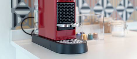 A red espresso machine with a black control panel and a circular button on top, placed on a white countertop.