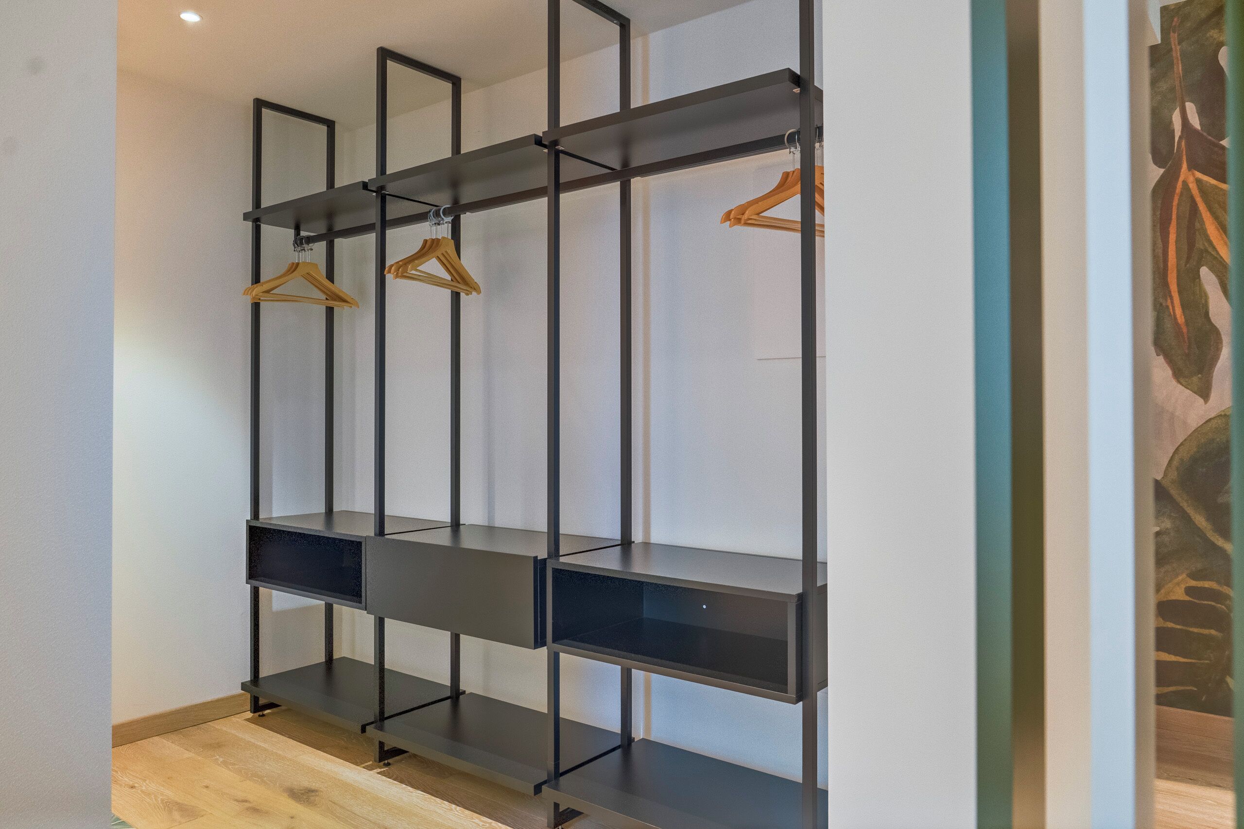 A modern, minimalist closet with black metal shelving and wooden hangers.