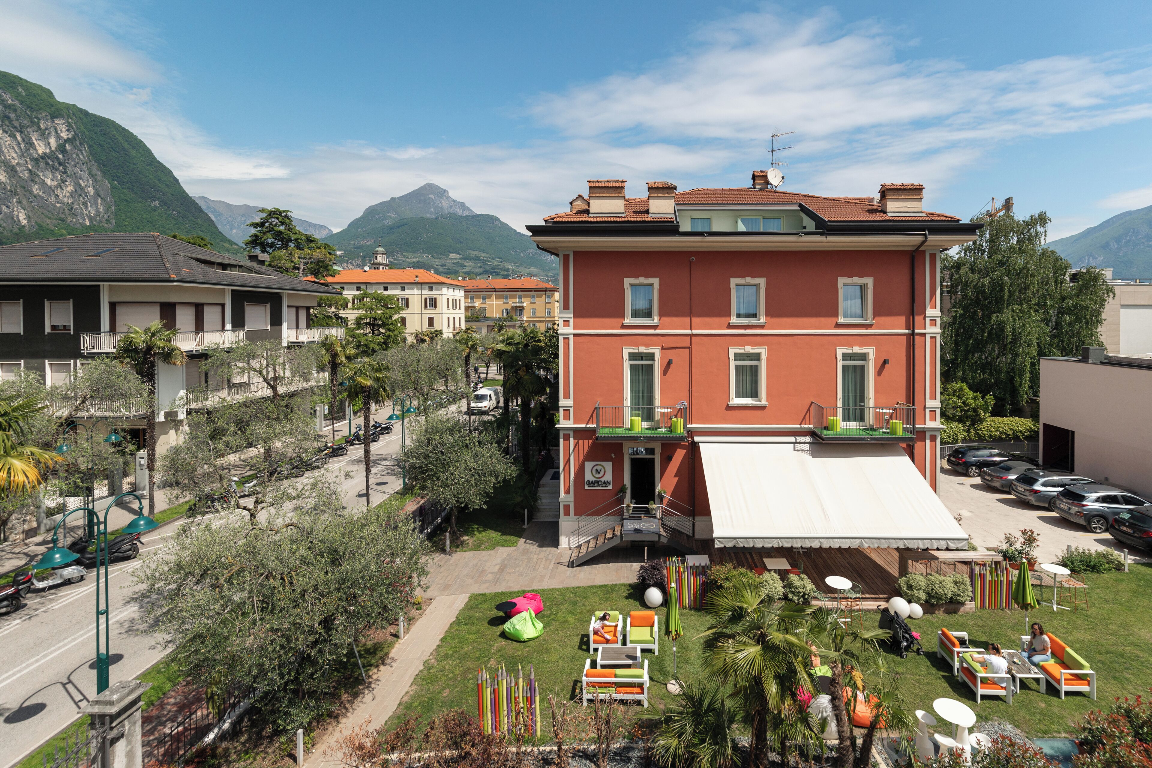 A multi-story building with a red facade, a balcony, and a covered outdoor seating area with tables and chairs.