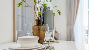 Ein Esstisch, gedeckt mit Tellern, Schüsseln, Besteck und einer Vase mit Grünpflanzen.