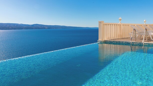 Una piscina cristallina con vista sul mare e colline lontane.