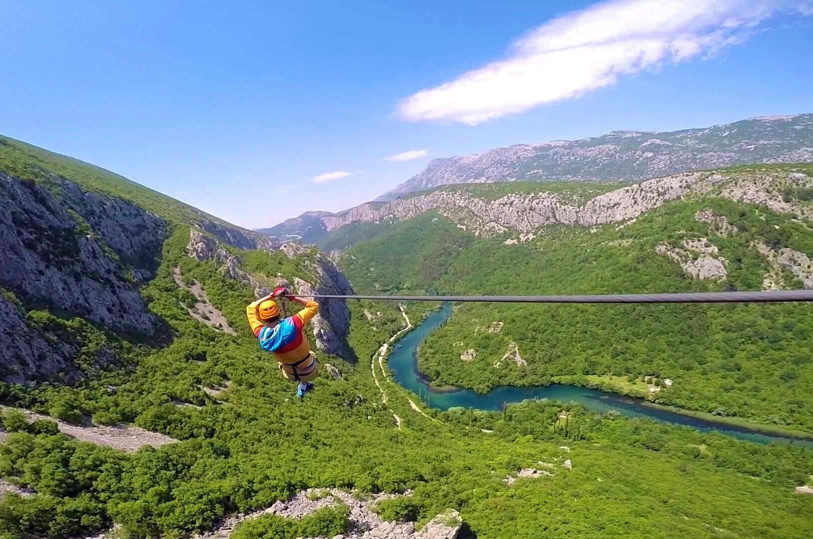 Una persona haciendo bungee jumping desde un risco alto, con un río y montañas al fondo.