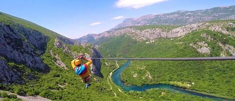 Una persona haciendo bungee jumping desde un risco alto, con un río y montañas al fondo.