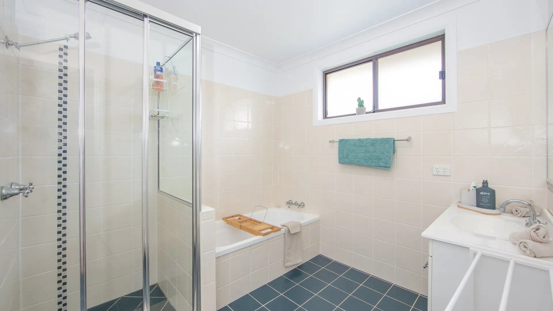 A bathroom with a glass-enclosed shower, a bathtub, a sink, and a window above the mirror.