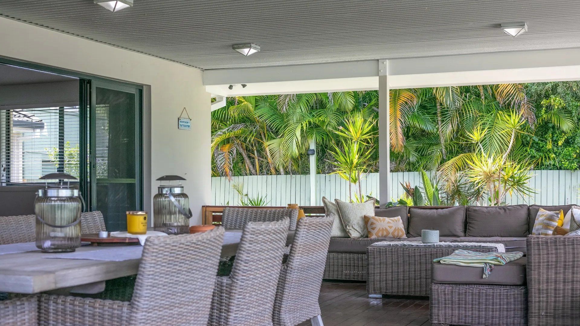 An outdoor patio with wicker furniture, a table with candles, and a view of tropical plants.