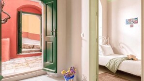 A room with a bed, a small table, and a vase with flowers. - Traditonal House in Symi (Simi)