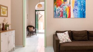 A living room with a brown sofa, a colorful abstract painting, a wicker chair, and a white cabinet. - Traditonal House in Symi (Simi)