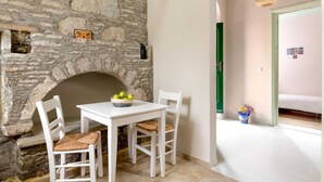 A stone wall with a fireplace, a white table with chairs, and a green door. - Traditonal House in Symi (Simi)