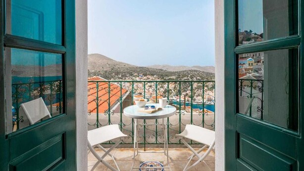 A balcony with a table and chairs, overlooking a town and mountains. - Traditonal House in Symi (Simi)