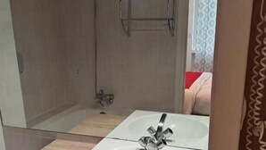 A bathroom with a white sink, a mirror above it, and a shower area visible in the background. - Hôtel les nouveaux Ambassadeurs (Saint-Chamond)