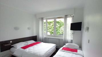 Ein Hotelzimmer mit zwei Betten, einem Schreibtisch, einem Stuhl, einem Fernseher und einem Fenster mit Blick auf Bäume.
