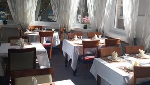 A restaurant with white tablecloths, wooden chairs, and white curtains. - Hôtel les nouveaux Ambassadeurs (Saint-Chamond)