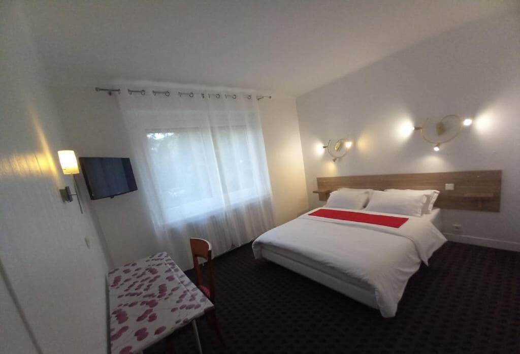 A hotel room with a bed, a desk, a chair, a TV, and a window with curtains.