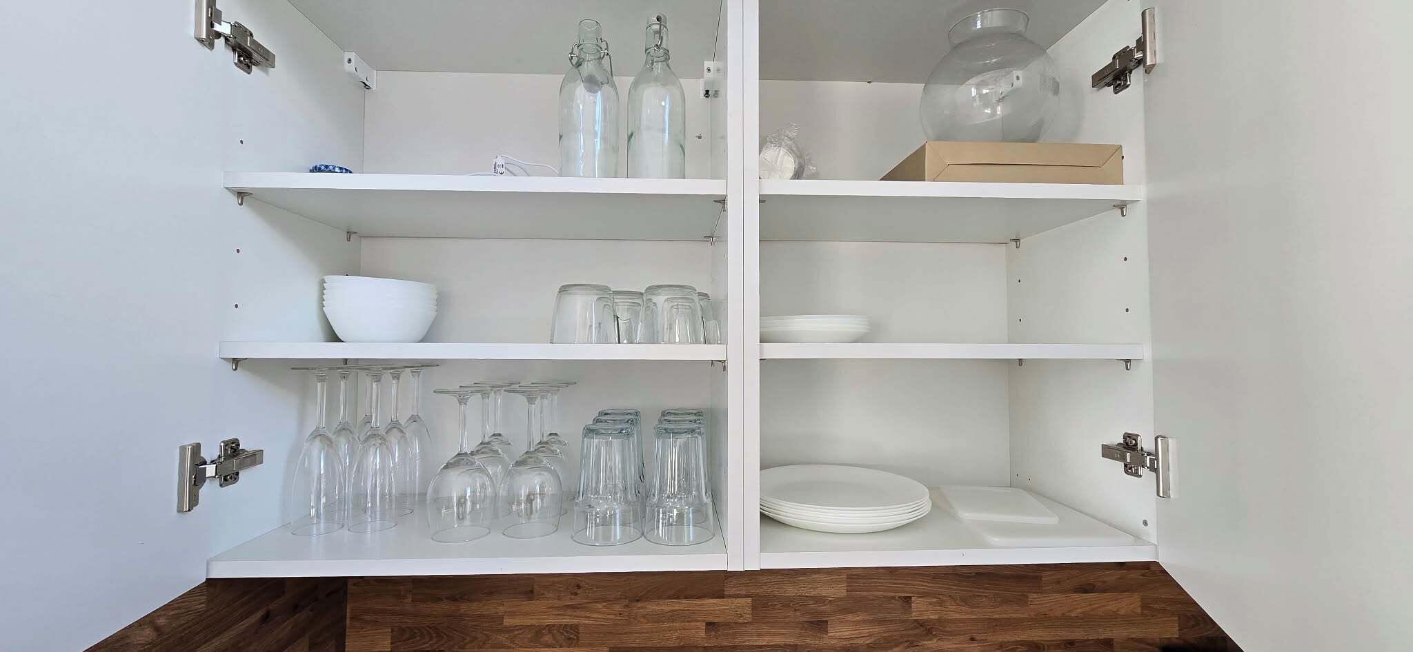 A white cabinet with shelves holding glassware, bowls, and plates.