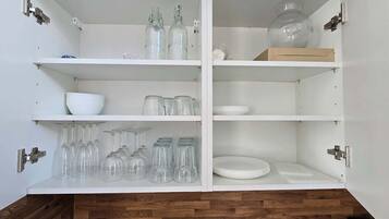 A white cabinet with shelves holding glassware, bowls, and plates.
