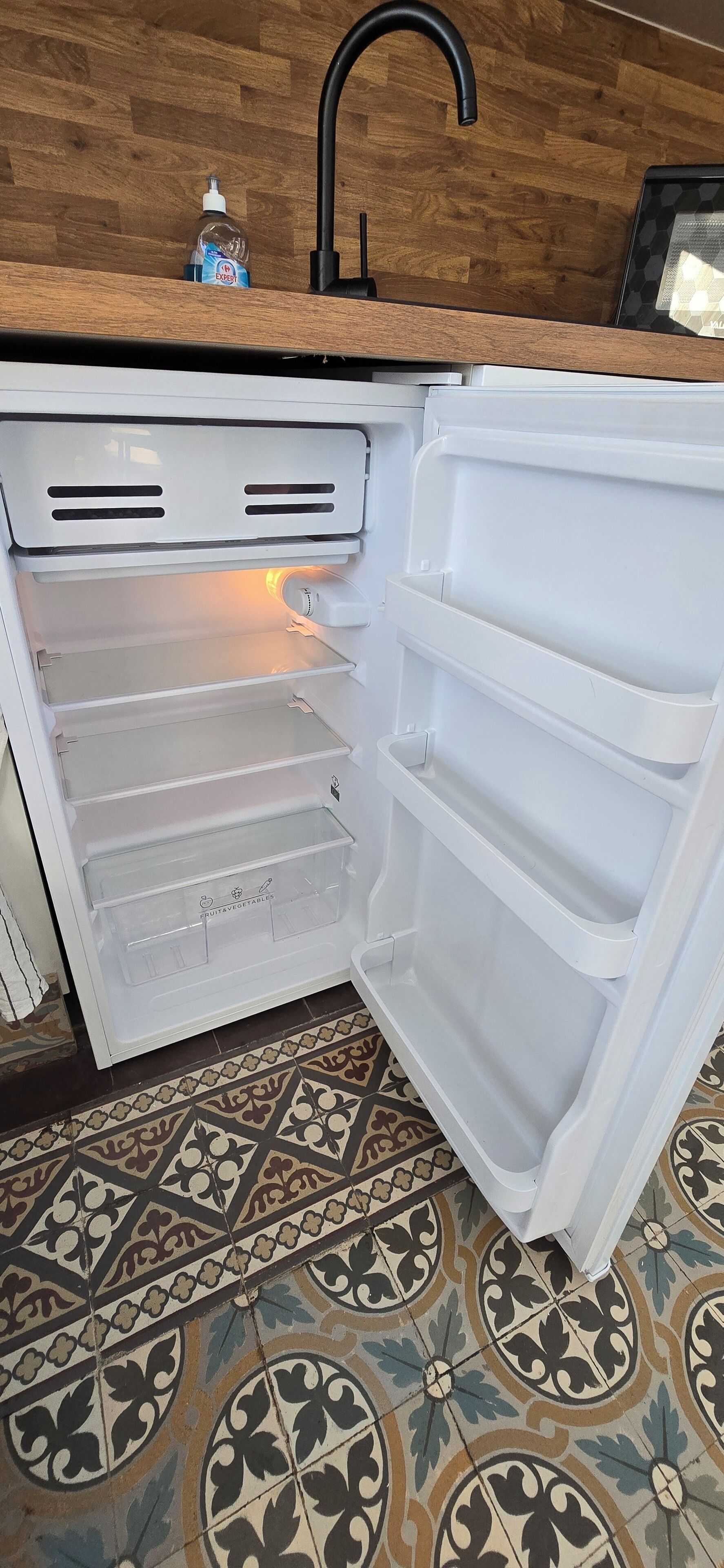 An open refrigerator with multiple shelves and a bottle of dish soap on the countertop.