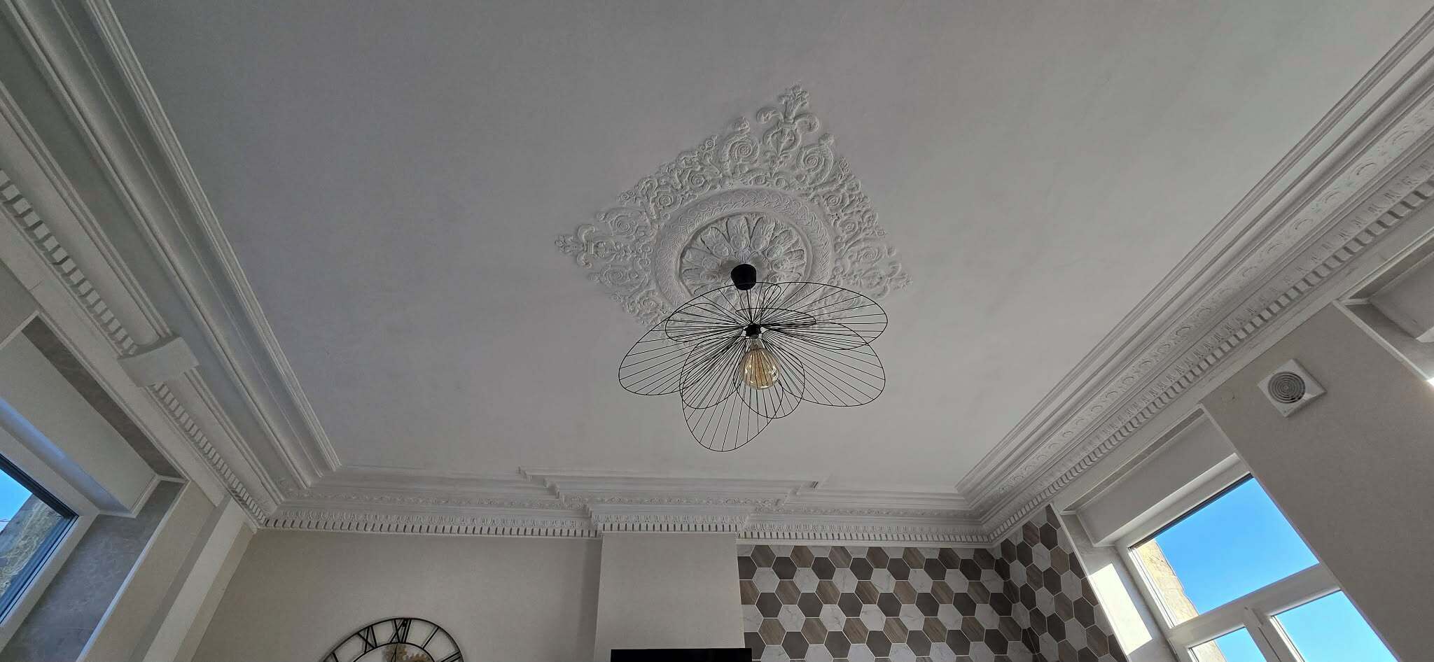 Ein Zimmer mit einer verzierten Decke, einer Uhr und einer Wand mit Muster.