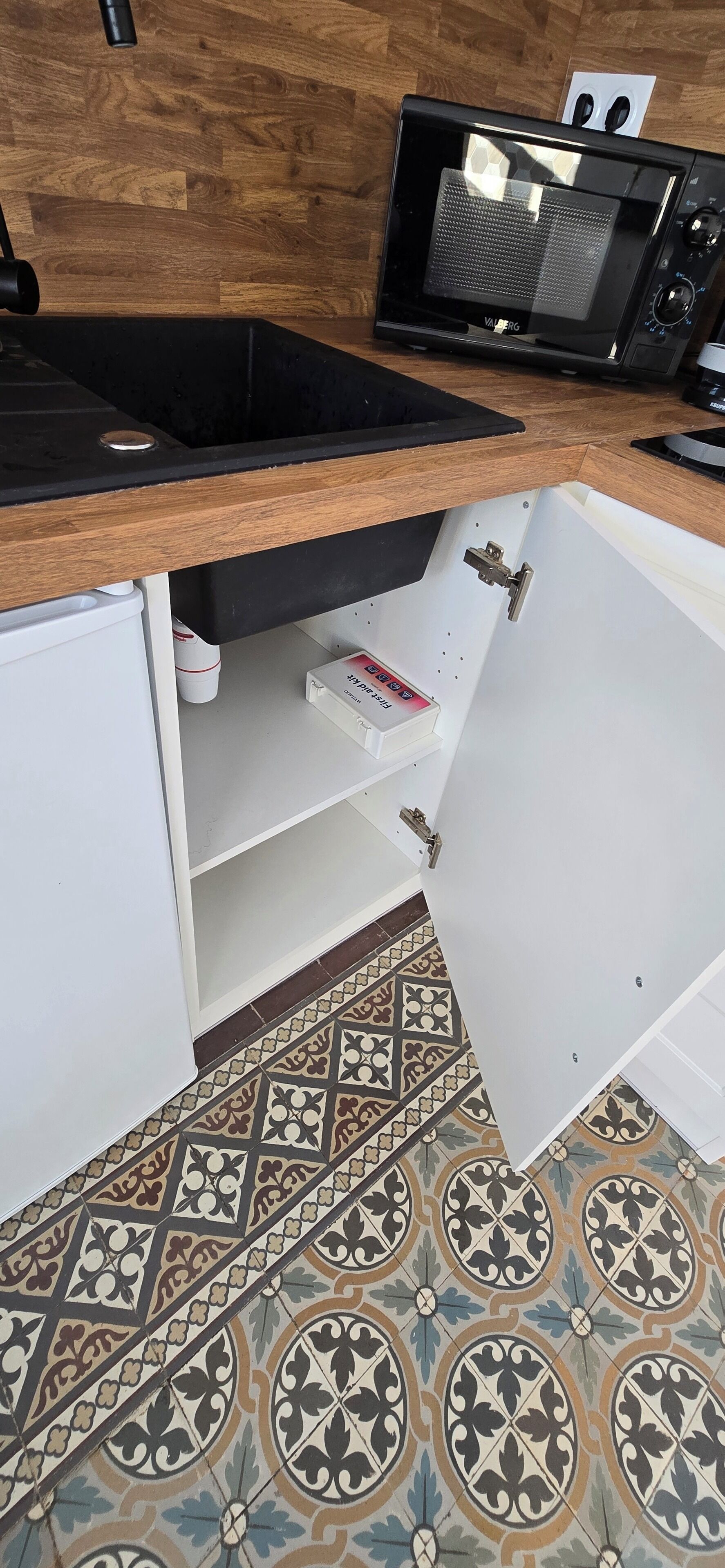 A kitchen with a wooden countertop, a black microwave, and a patterned tile floor.
