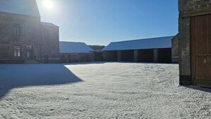 Een besneeuwde binnenplaats met gebouwen, een houten deur en een heldere lucht.