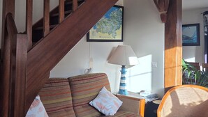 Eine Holztreppe führt zu einer oberen Etage, ein gestreifter Schlafsofa mit Kissen, eine Lampe und eine gerahmte Karte an der Wand.